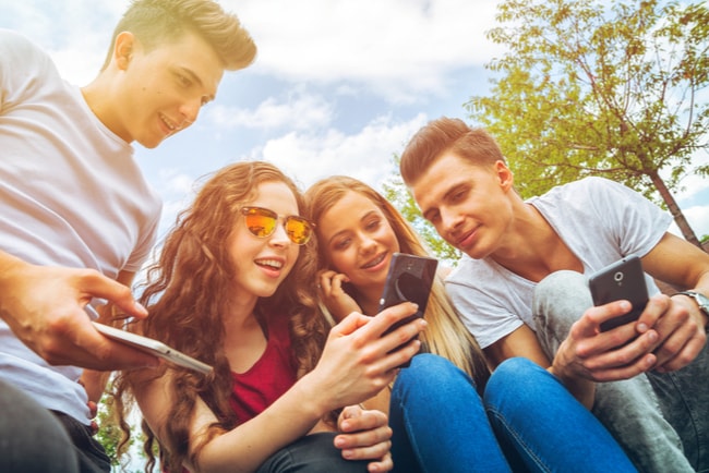 fyra vänner med telefon surfar på internet utomhus